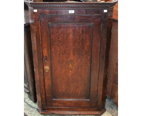 A George III oak wall hanging corner cupboard, dentil cornice above a panel door inlaid with a musical trophy, 104cm high