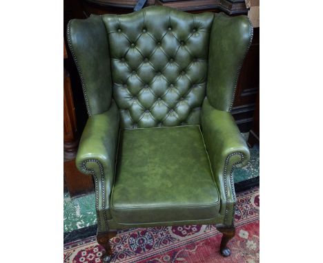 A Chesterfield type wingback armchair, deep button back, scroll arm, pad forefeet