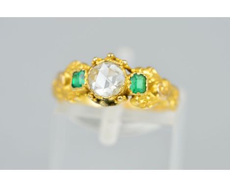 A LATE GEORGIAN GOLD DIAMOND AND EMERALD RING, the central rose cut diamond flanked by rectangular cut emeralds to the scroll