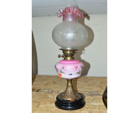 AN EARLY 20TH CENTURY OIL LAMP with a pink glass reservoir above an Art Nouveau panelled stand, complete with lamp shade and 