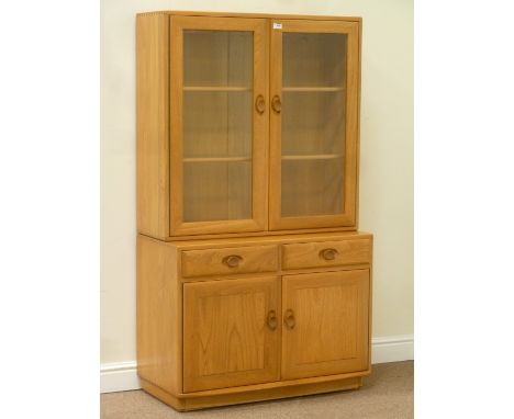 Ercol light elm display cabinet enclosed by two glazed doors fitted with adjustable shelves, above two drawers and double cup