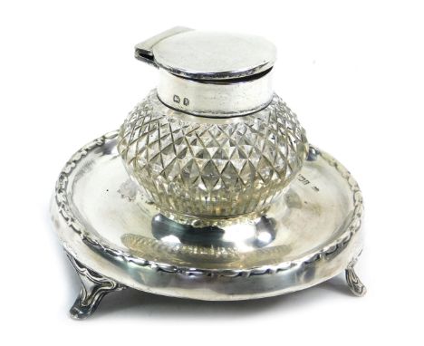 A George V silver inkwell, with central pressed glass inkwell, on a circular tripod base, hallmarks rubbed, 10cm diameter. 