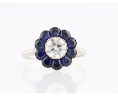 A diamond and sapphire flower design ring, set with a central transitional cut diamond, measuring approx. 0.75ct, surrounded 