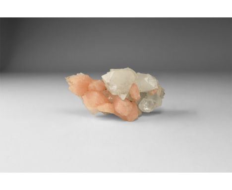 A cluster of white semi-transparent apophyllite and pale orange stilbite crystals, in white card tray with label reading: 'AP
