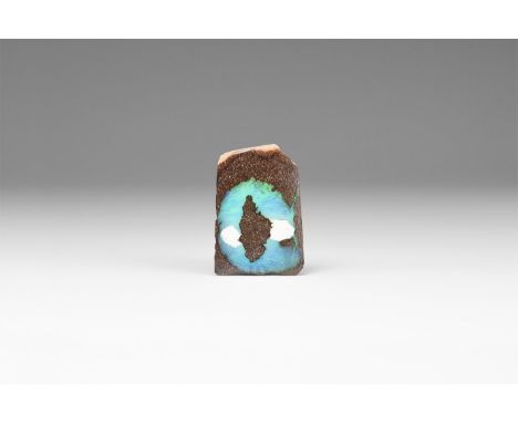 A cut slice of red-brown sandstone with circular area of precious opal diffracting light in primarily blues and greens, in wh