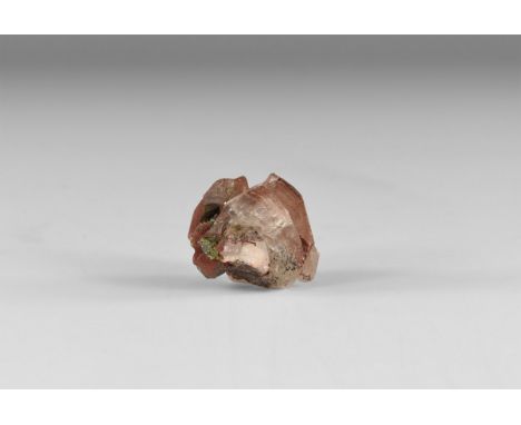 A calcite crystal with red oxide colouring and sphalerite growths to one end, in white card tray with label reading: 'CALCITE