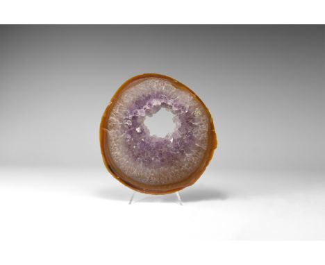 A cut and polished agate geode slice with band of brown to the outer border and opened centre framed by amethyst crystals. 33