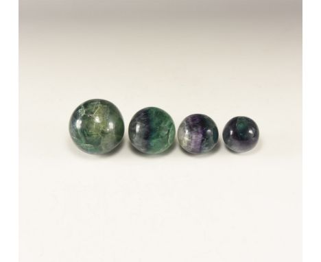A group of four polished purple and dark green fluorite spheres in graduating sizes. 850 grams total, 39-60mm (1 1/2 - 2 1/4"