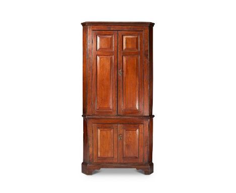 A George III elm standing corner cupboard
In two parts, the moulded cornice above a pair of fielded panelled doors enclosing 