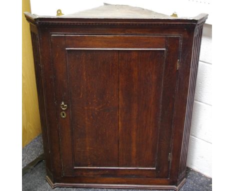 A George III oak splay front wall mounted corner cabinet, outswept cornice, dentil frieze, panel doo enclosing shaped shelvin