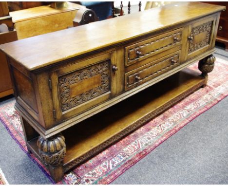 A Priory style oak sideboard, oversailing top, two drawers flanked by carved panel door cupboards, cup and cover forelegs, un