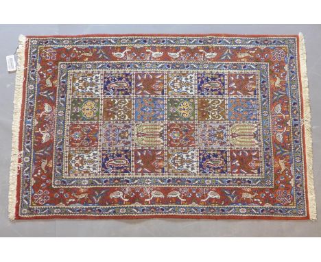 A Persian rug with repeating tile design with stylised floral motifs, within border with flowers, birds and animals on a roug
