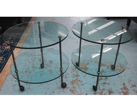 CIRCULAR LAMP TABLES, a pair, glass with undertier on castors, 60cm x 60cm H. (2)