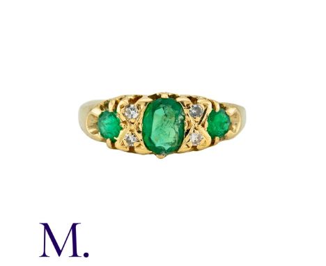 An Emerald And Diamond Ring in 18k yellow gold, set with a principal oval cut emerald, and two round cut emeralds, punctuated