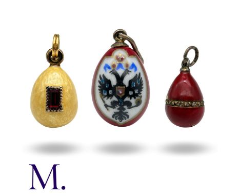 A Collection of Three Russian Enamel Eggs, one with yellow enamel and set either side with a red emerald cut stone (2.1cm, 6.