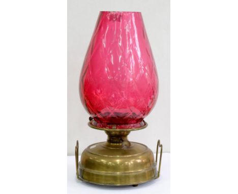 A BRASS OIL LAMP WITH WIRE HANDLES AND TRELLIS MOULDED CRANBERRY GLASS TAPERED SHADE, 48CM H, 20TH C