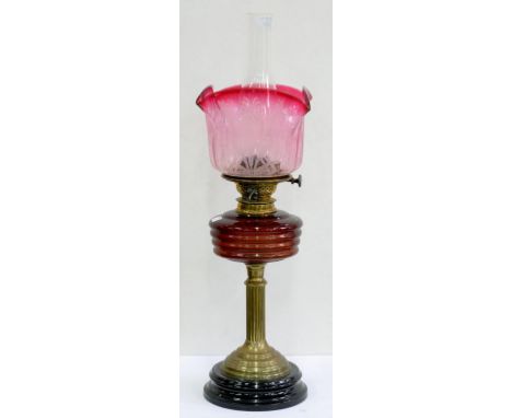 AN EDWARDIAN BRASS OIL LAMP, WITH REEDED PILLAR AND BASE, RUBY GLASS FOUNT, BRASS BURNER AND CRANBERRY SHADED AND ETCHED GLAS
