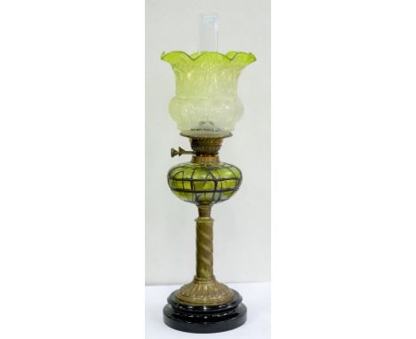 AN EDWARDIAN BRASS SPIRALLY FLUTED OIL LAMP WITH IRIDESCENT TRAILED GREEN GLASS FOUNT, BRASS BURNER AND GREEN SHADED AND ETCH