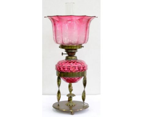 AN EDWARDIAN BRASS OIL LAMP WITH DETACHABLE SPIRALLY LOBED CRANBERRY GLASS FOUNT, WITH BRASS BURNER AND CRANBERRY SHADED AND 