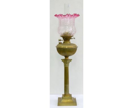 AN EDWARDIAN BRASS COLUMNAR OIL LAMP WITH REEDED BRASS FOUNT AND A CRANBERRY FLASHED AND MOULDED GLASS SHADE, 71CM H EXCLUDIN