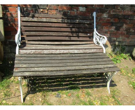 A two seat garden bench with weathered timber lathes raised on a pair of decorative painted cast alloy end supports 126 cm wi