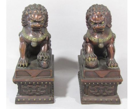 A pair of Chinese bronze and lacquered lion dogs with raised paws, set on plinths, 15 cm wide x 20 cm high 
