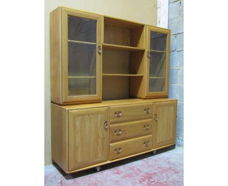 An Ercol light elm cabinet, the lower sideboard section enclosed by three central doors flanked by two cupboards, the upper s