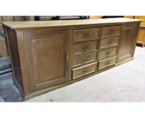 A long and low light oak dresser base partially enclosed by a pair of rectangular moulded panelled doors flanking two towers 