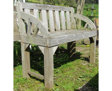 A weathered hardwood two seat garden bench with slatted seat, back and curved arms (stamped to back rail www.chieftradingpost