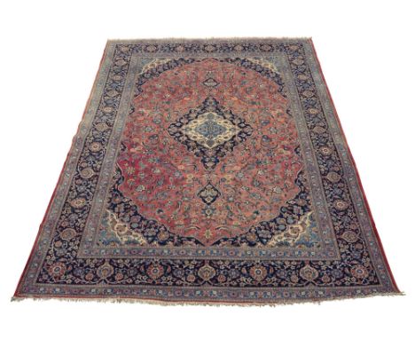 A Tabriz carpet, with indigo and ivory pole medallion in brick red field with floral and foliate decoration, with indigo main