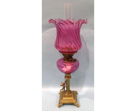 A Victorian brass column oil lamp, the column with winged cherub on square base and scroll feet, with cranberry glass reservo