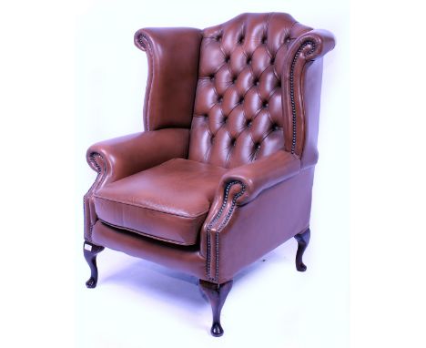 A 20TH CENTURY LEATHER UPHOLSTERED WING ARMCHAIR with button upholstered back and studded details standing on cabriole legs, 