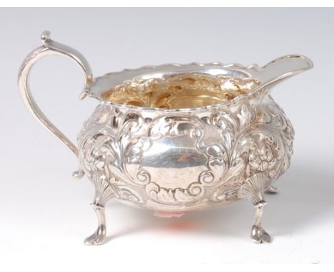 A late Victorian silver cream jug, of squat circular form, having twin vacant cartouches within a leaf chased surround, 7.2oz