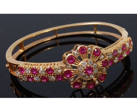 A yellow metal, ruby and diamond set hinged bangle, arranged as a pierced flower head with centre round cut claw set ruby wei