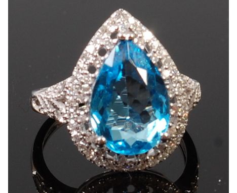 A contemporary 14ct white gold, blue topaz and diamond set dress ring, the pear cut three claw set topaz within a two-tier di