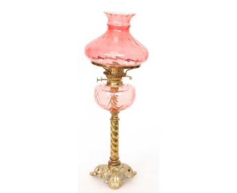 A Victorian brass oil lamp with cast foliate base and cranberry reservoir and shade, height 66cm