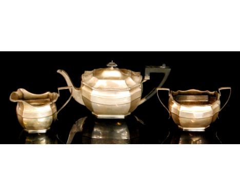 A hallmarked silver three piece tea service comprising teapot, sugar bowl and cream jug, each with canted corners and reeded 