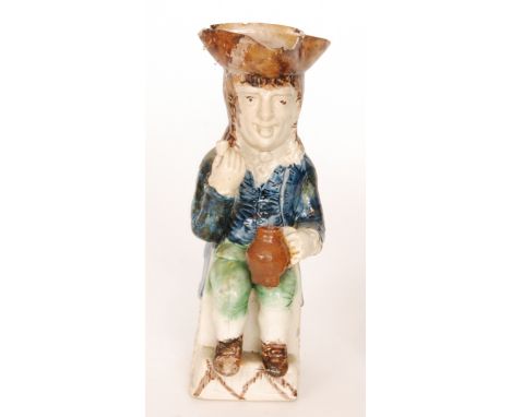 A 19th Century Staffordshire Thin Man Toby jug, seated wearing a blue frock coat and green breaches holding a jug and a pipe,