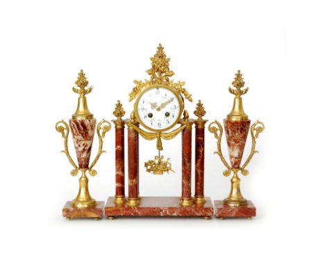 An early 20th Century French rouge marble and gilt metal mounted clock garniture, the portico style clock with a white enamel