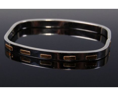 A contemporary hinged white metal bangle, with raised yellow metal detail 