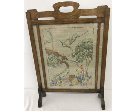 A vintage oak fire screen with needlework panel behind glass.  