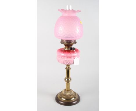 A Victorian oil lamp with pink glass reservoir and shade, on brass pillar
