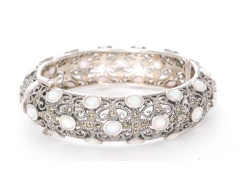 A continental silver opal and marcasite pierced bangle detailed with thirty eight collar set opals terminating in tongue and 