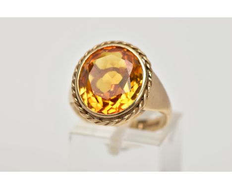 A 9CT GOLD SYNTHETIC ORANGE SAPPHIRE DRESS RING, designed with a large oval cut synthetic orange sapphire, approximate dimens