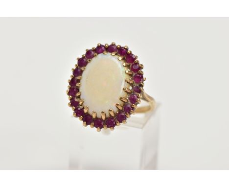 A YELLOW METAL OPAL AND RUBY CLUSTER RING, large cluster centring on an oval cut opal cabochon, within a circular cut ruby su