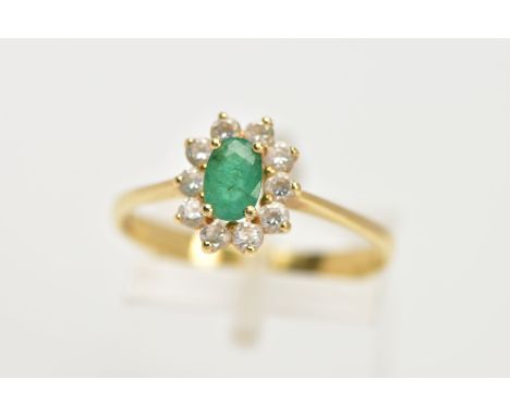 A YELLOW METAL EMERALD AND CUBIC ZIRCONIA CLUSTER RING, centring on a claw set, oval cut emerald, within a circular cut colou