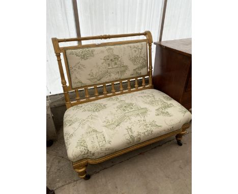 A VICTORIAN GOLD PAINTED LOW TWO SEATER SETTEE ON TURNED AND FLUTED LEGS AND UPRIGHTS, HAVING ORIENTAL DESIGN UPHOLSTERY 