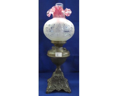 Early 20th Century brass double burner oil lamp, having brass reservoir on foliate cast metal base, etched glass shade and cl