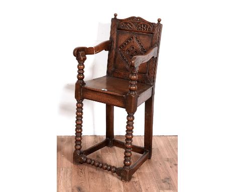 An oak Jacobean revival Wainscot style child's high chair, with decorative scroll cornice above chip carved lozange panel bac