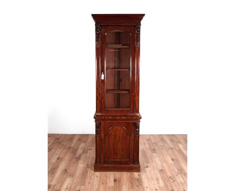 A Victorian carved mahogany bookcase, of narrow proportions, with ogee cornice above an arched glazed door, arched panel door